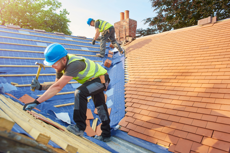 Two men performing residential roofing services, using hammers to work on a roof for Mr. Max Roofing.