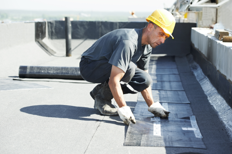 A man in a hard hat and safety glasses installs flat roof insulation for Mr. Max Roofing, ensuring safety and quality.