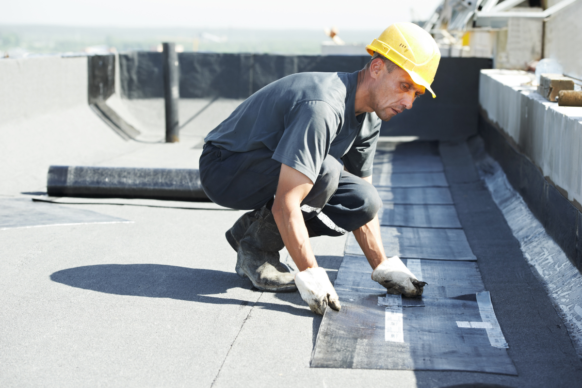 A man in a hard hat and safety glasses installs flat roof insulation for Mr. Max Roofing, ensuring safety and quality.
