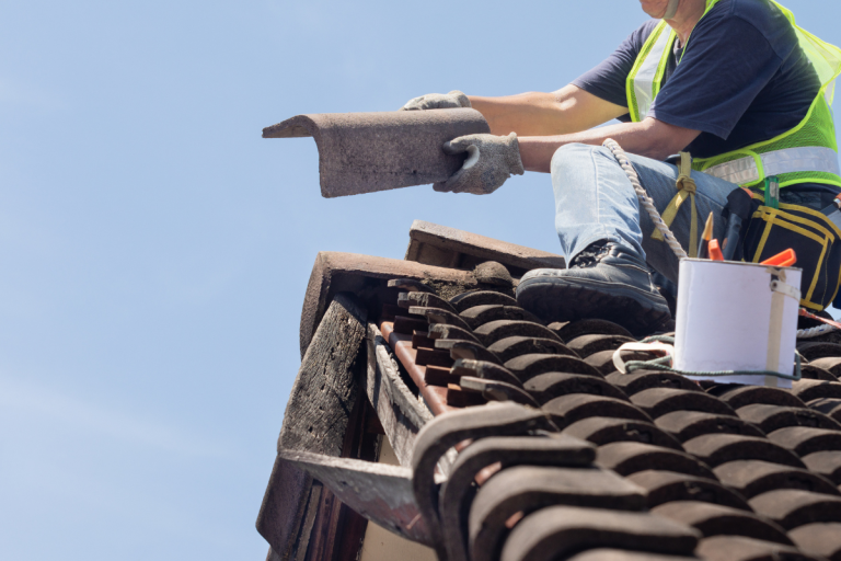 A man using a tool to work on a roof, representing Mr. Max Roofing's roof replacement cost services.
